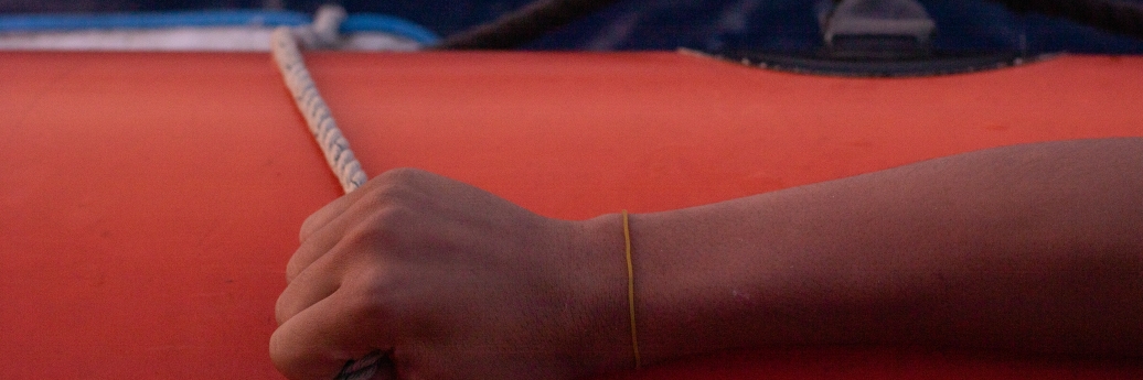 Een hand houdt het touw op een rode reddingsboot vast. 