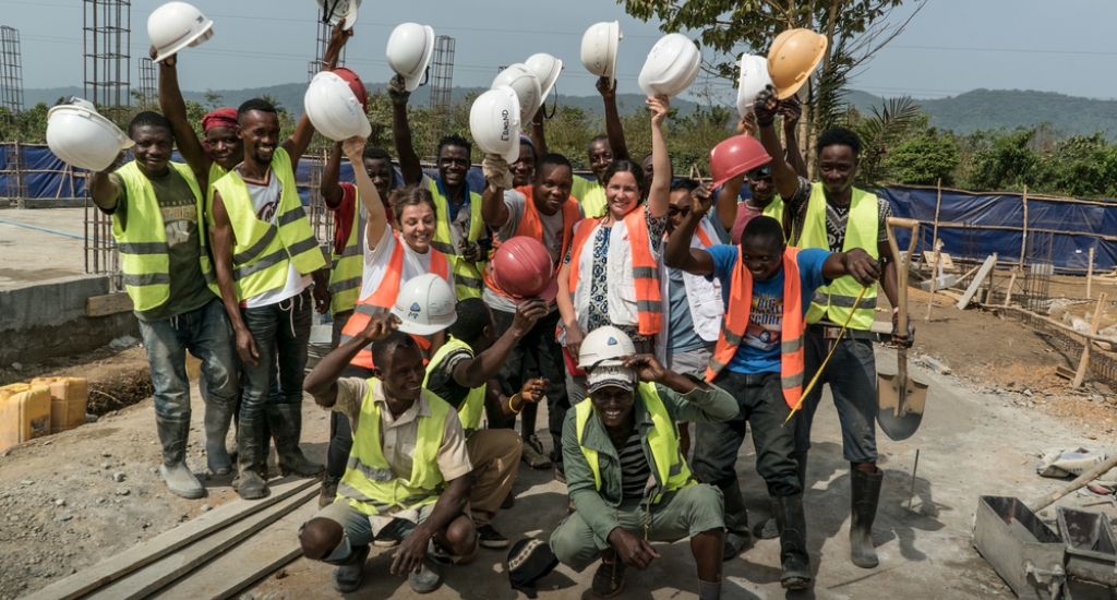 Workers on concrete buildings, including water and sanitation team members, pose at the construction site.